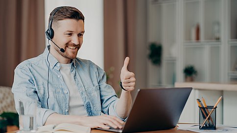 I like it. Glad bearded adult man has video conference keeps thumb up likes something focused at laptop computer has distance job interview dressed casually. Professional call center agent working